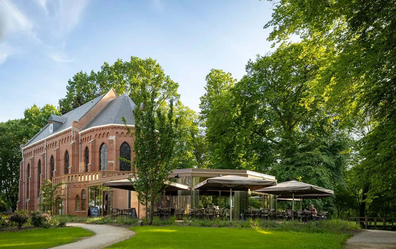 Het terras naast Kapel Montfort op Landgoed Bijstervelt in Oirschot, onder parasols tussen hoge bomen.